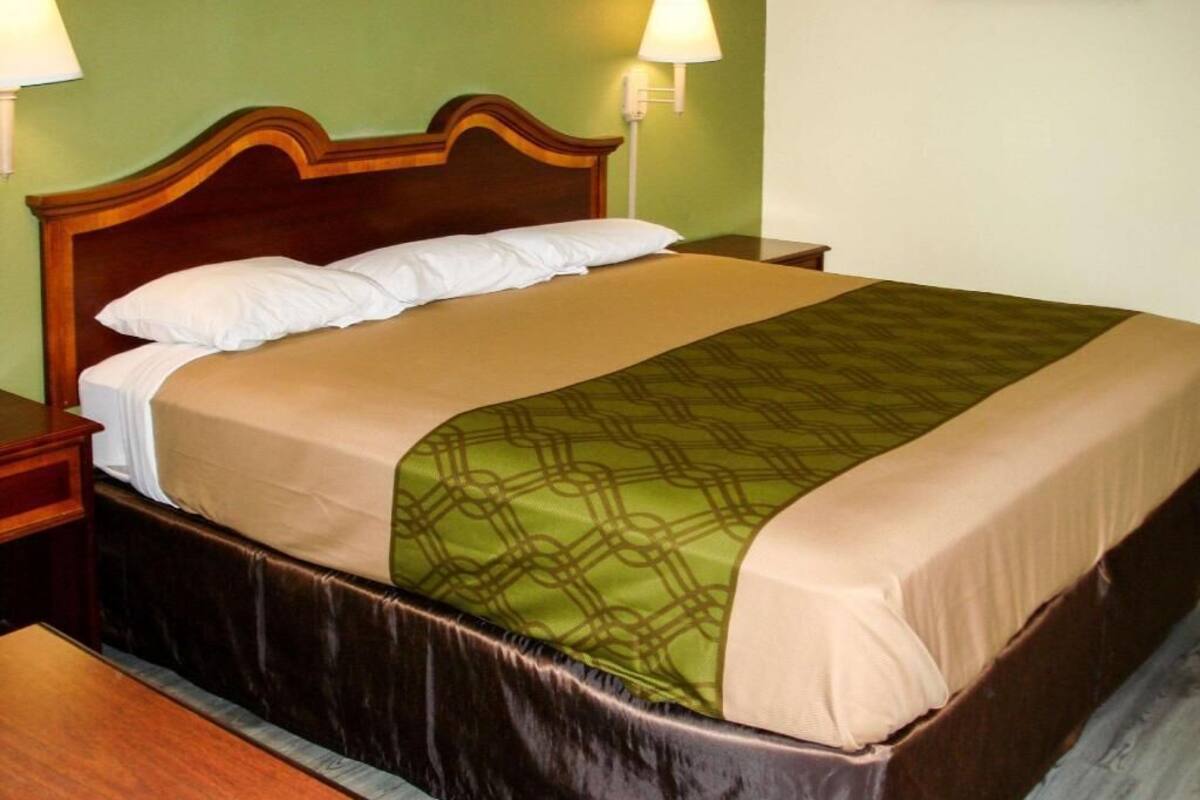 A bed with a wooden headboard, a green patterned bedspread, and a beige blanket.