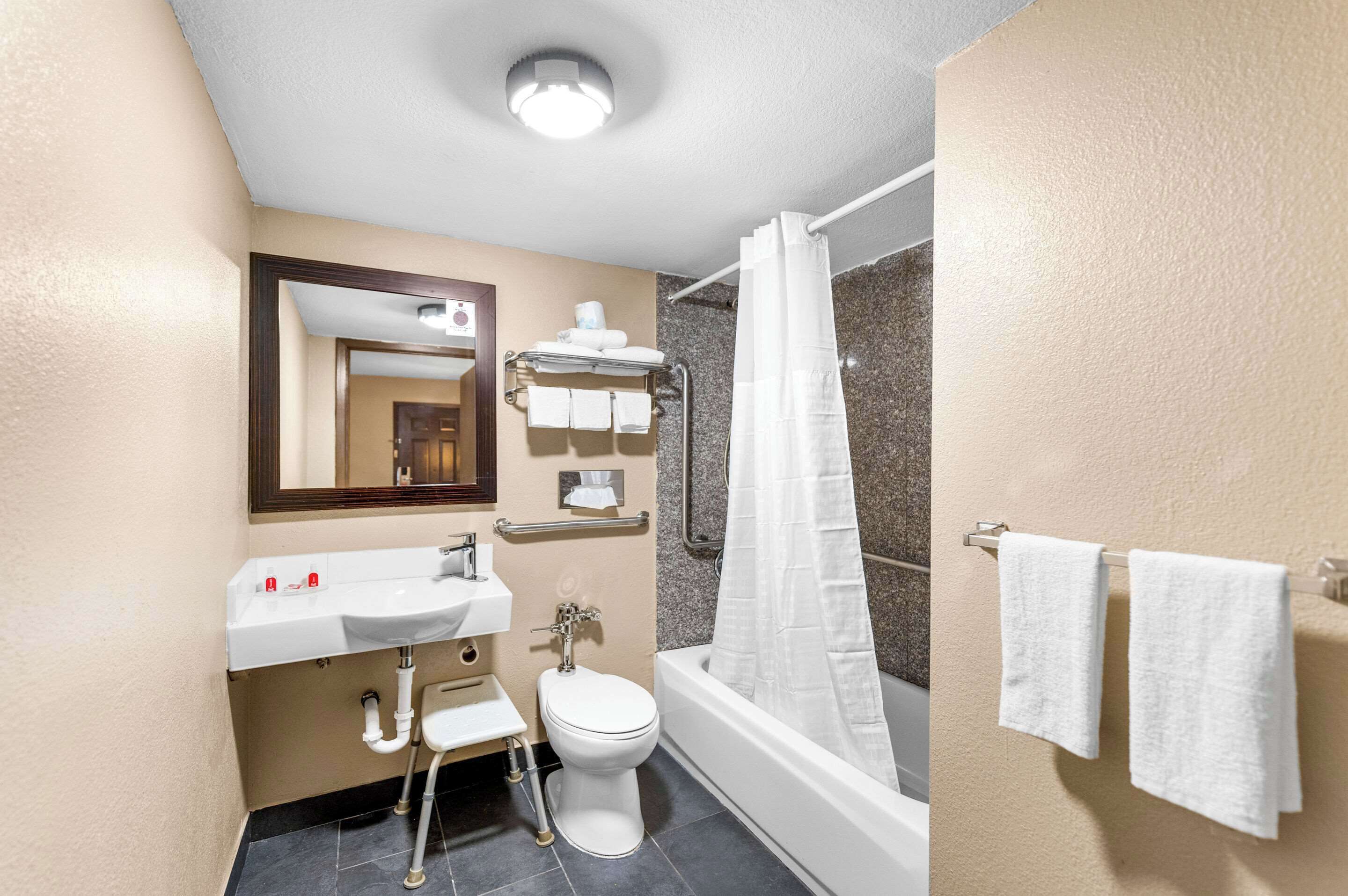A modern bathroom with a white sink, toilet, and bathtub. There is a mirror above the sink and a towel rack with two towels.