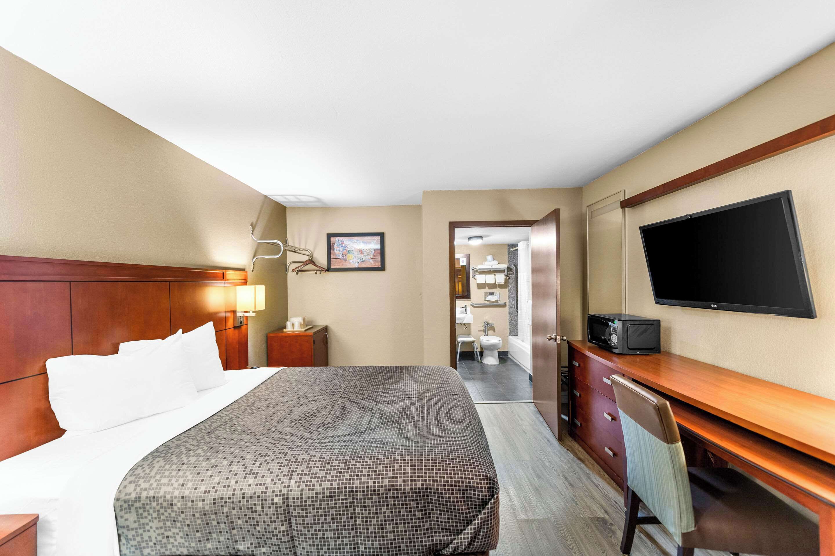 Habitación de hotel con cama, escritorio con televisor, lámpara y un cuadro en la pared.