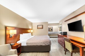 Habitación de hotel con cama, mesita de noche, lámpara, escritorio, silla, televisor y baño a la vista.