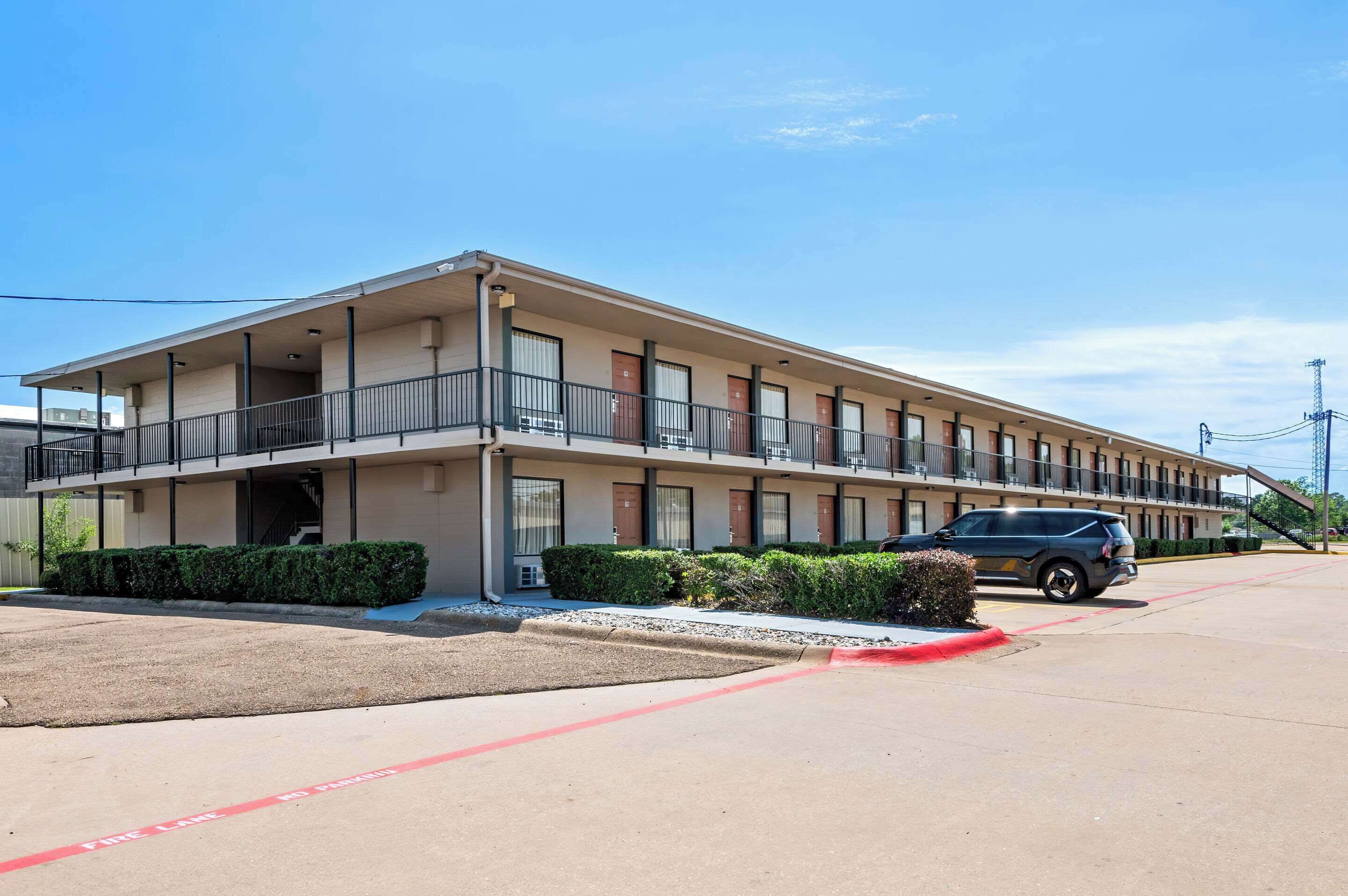 Un motel con una estructura de dos pisos, un área de estacionamiento techada y un edificio de un solo piso adyacente.