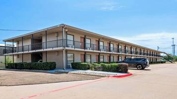 Un motel con una estructura de dos pisos, un área de estacionamiento techada y un edificio de un solo piso adyacente.