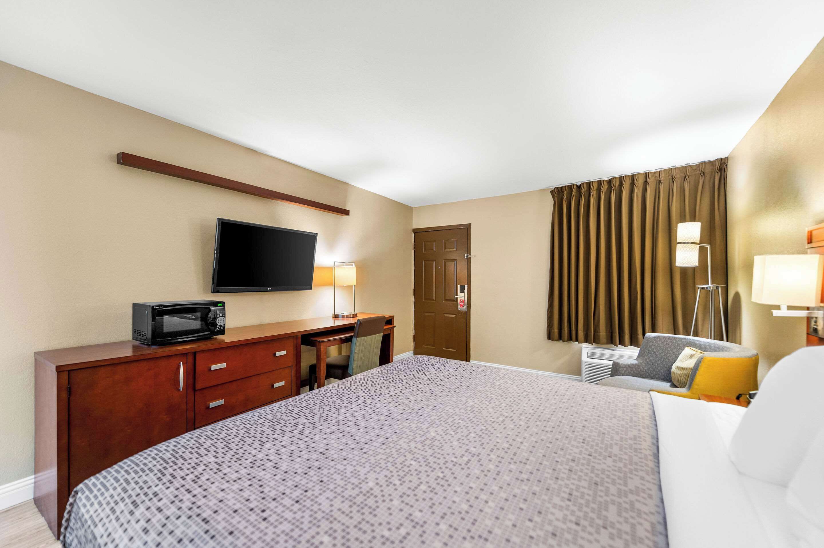 A hotel room with a bed, a desk with a television, a chair, and a lamp.