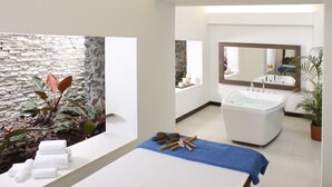 A spa room with a stone wall, a bathtub, a massage table, and a large mirror.
