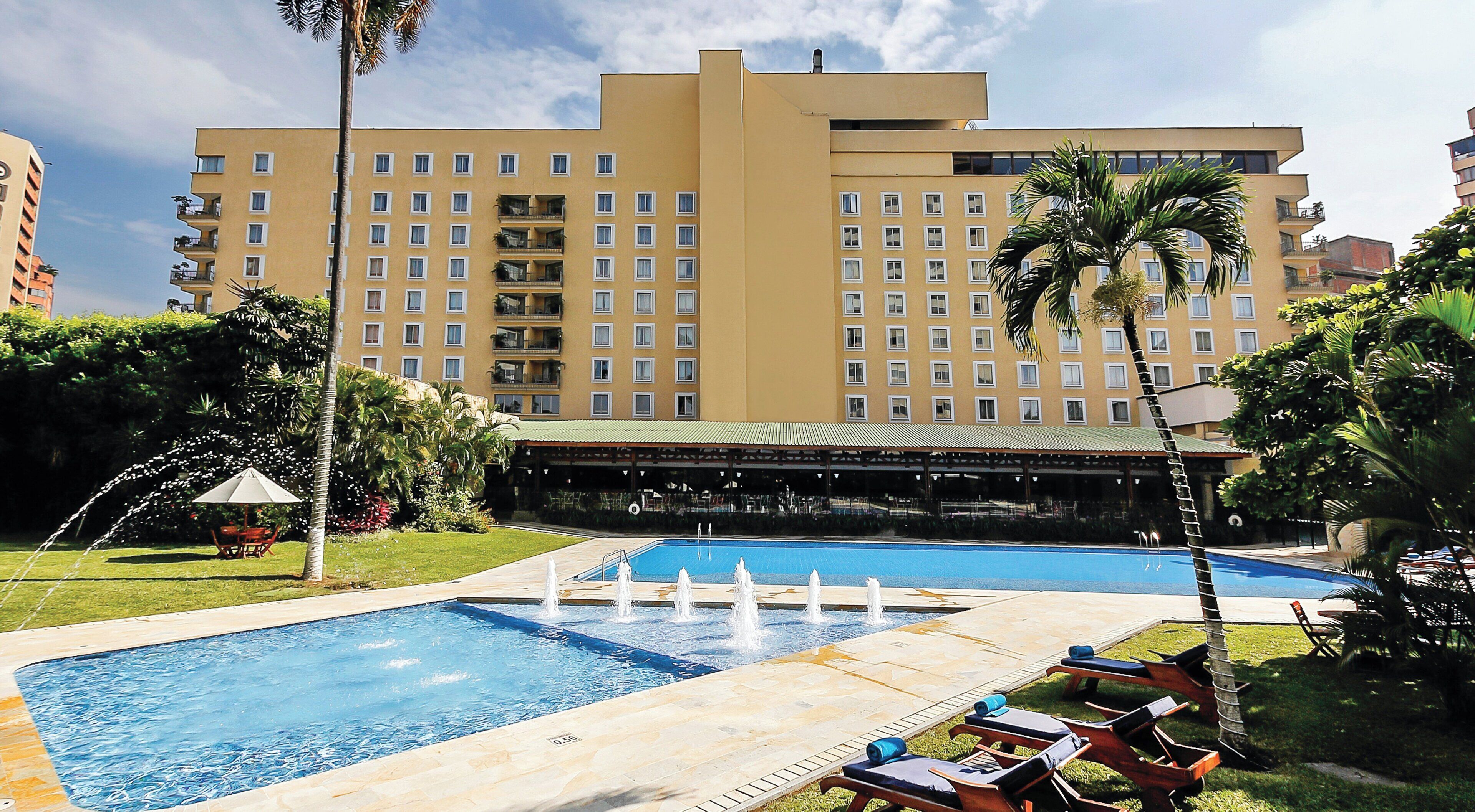Un hotel con piscina, sillas de descanso y una zona cubierta con mesas y sillas.