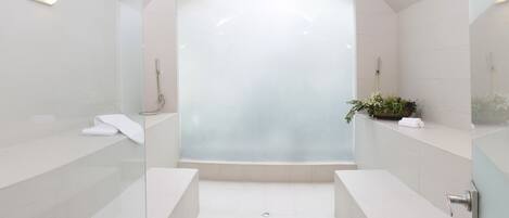 A modern bathroom with a glass-enclosed shower, white tiles, and a potted plant on the vanity.