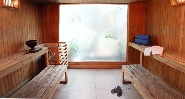 A sauna room with wooden benches, a bench with a towel, a bowl, and a shelf with towels.