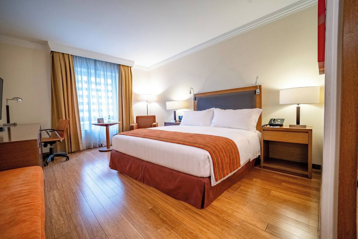 A hotel room with a large bed, bedside tables, a desk, and a chair.