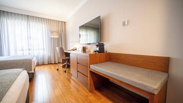 Habitación de hotel con un escritorio de madera, una cama, una silla, televisión y una ventana con cortinas.