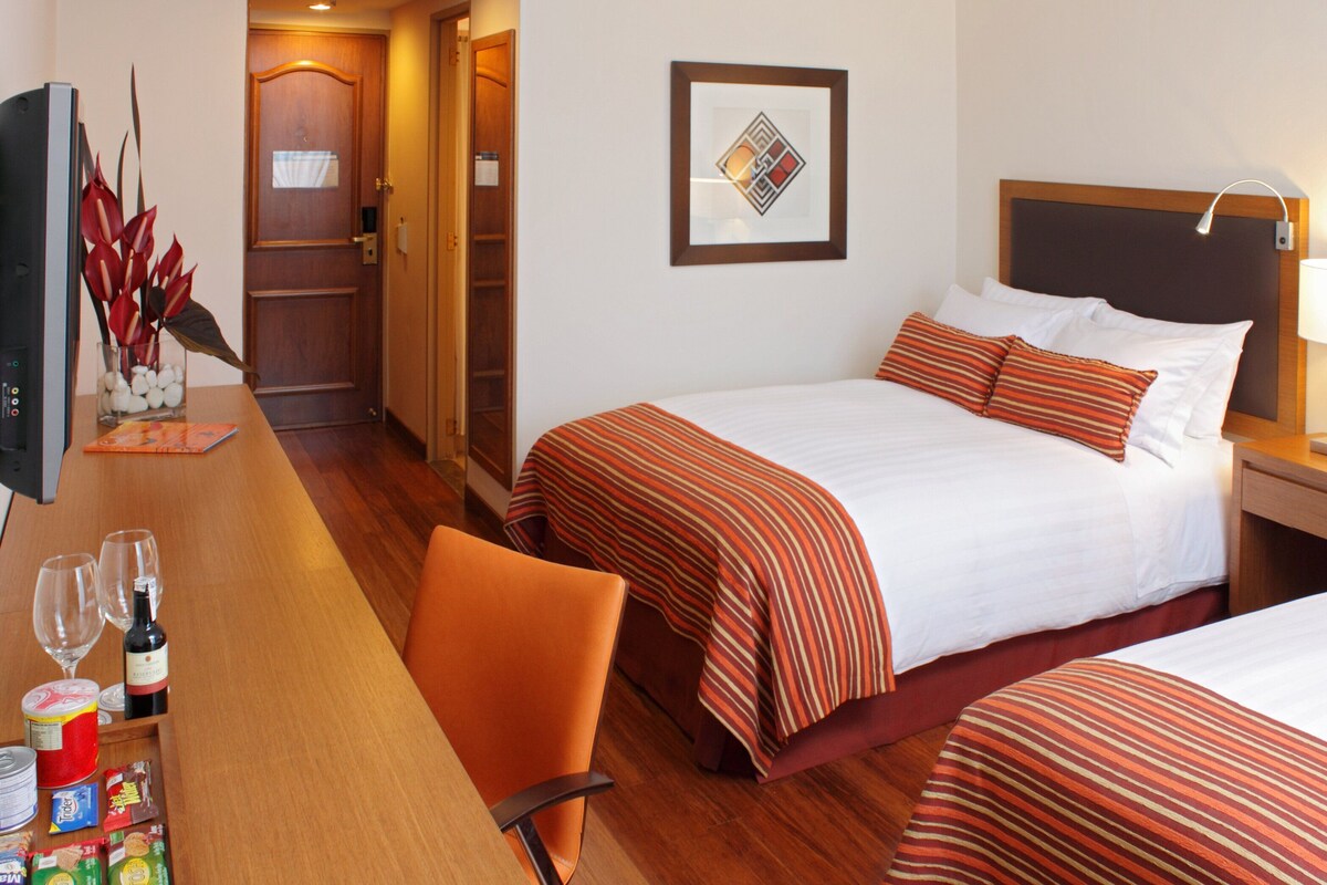 Une chambre d’hôtel avec deux lits, un bureau avec une chaise, une télévision et une porte.