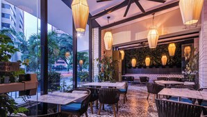 An indoor dining area with tables and chairs, large windows, and hanging pendant lights.