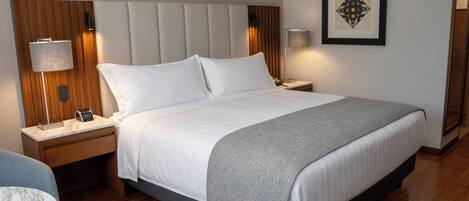 A hotel room with a large bed, two bedside tables, a nightstand, a lamp, a framed picture on the wall, and a chair.