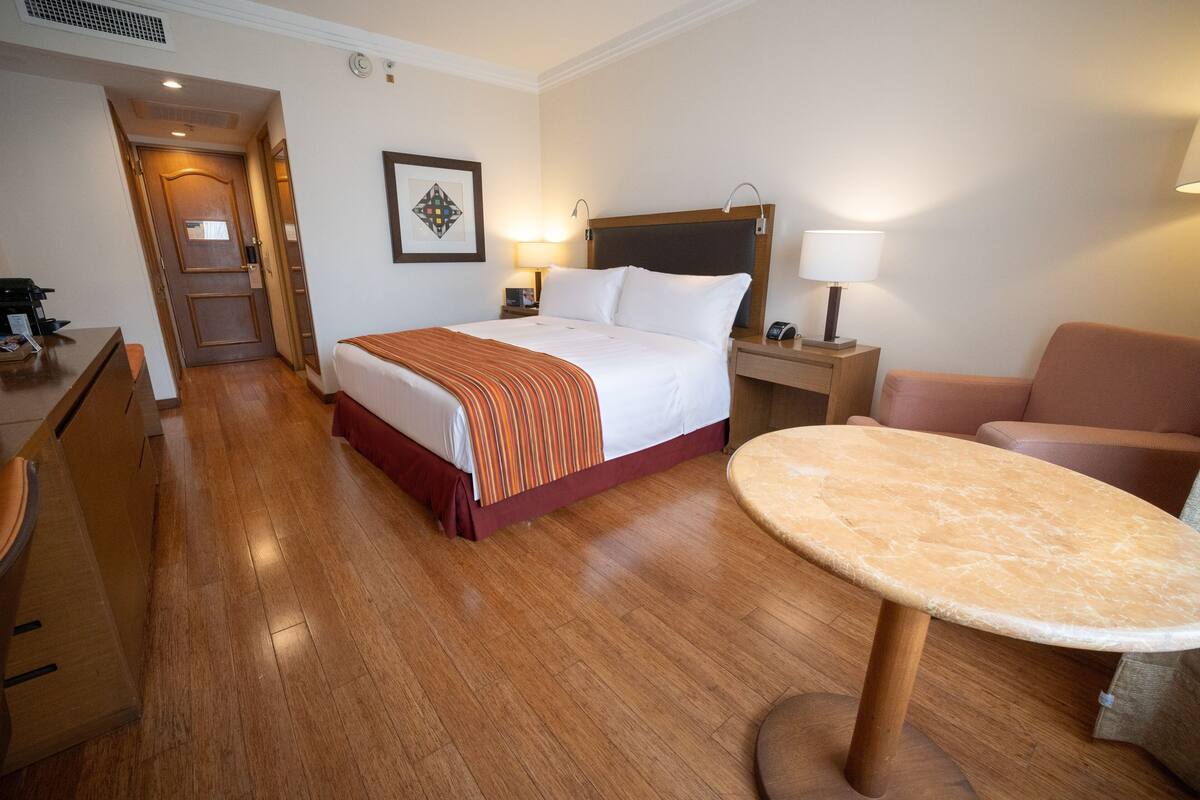 A hotel room with a bed, bedside tables, a desk, a chair, and a round table.