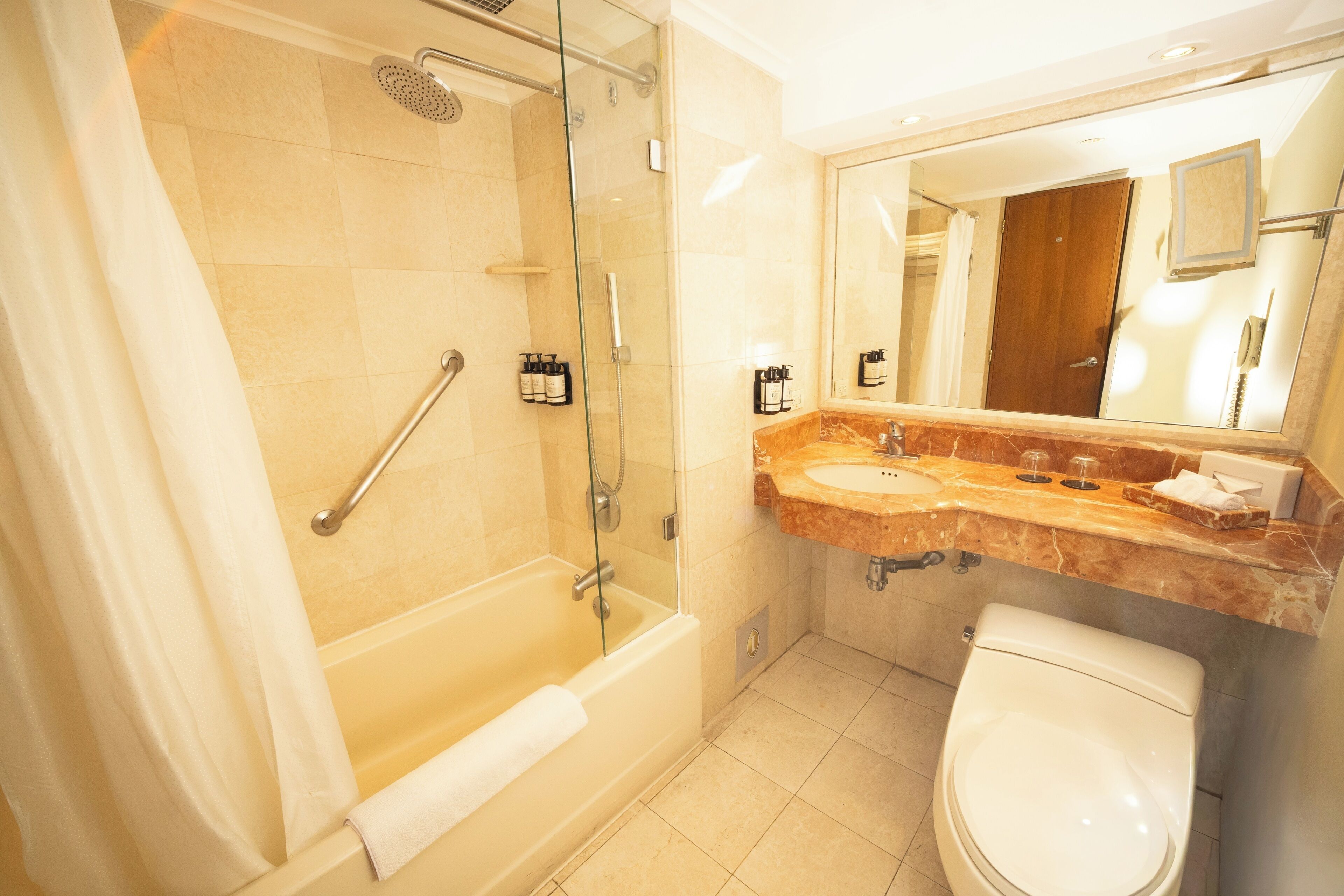 Un baño moderno con ducha envuelta en vidrio, bañera, inodoro y tocador con lavabo y espejo.