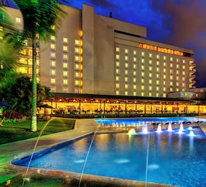 A hotel with a swimming pool, outdoor seating, and a well-lit facade.