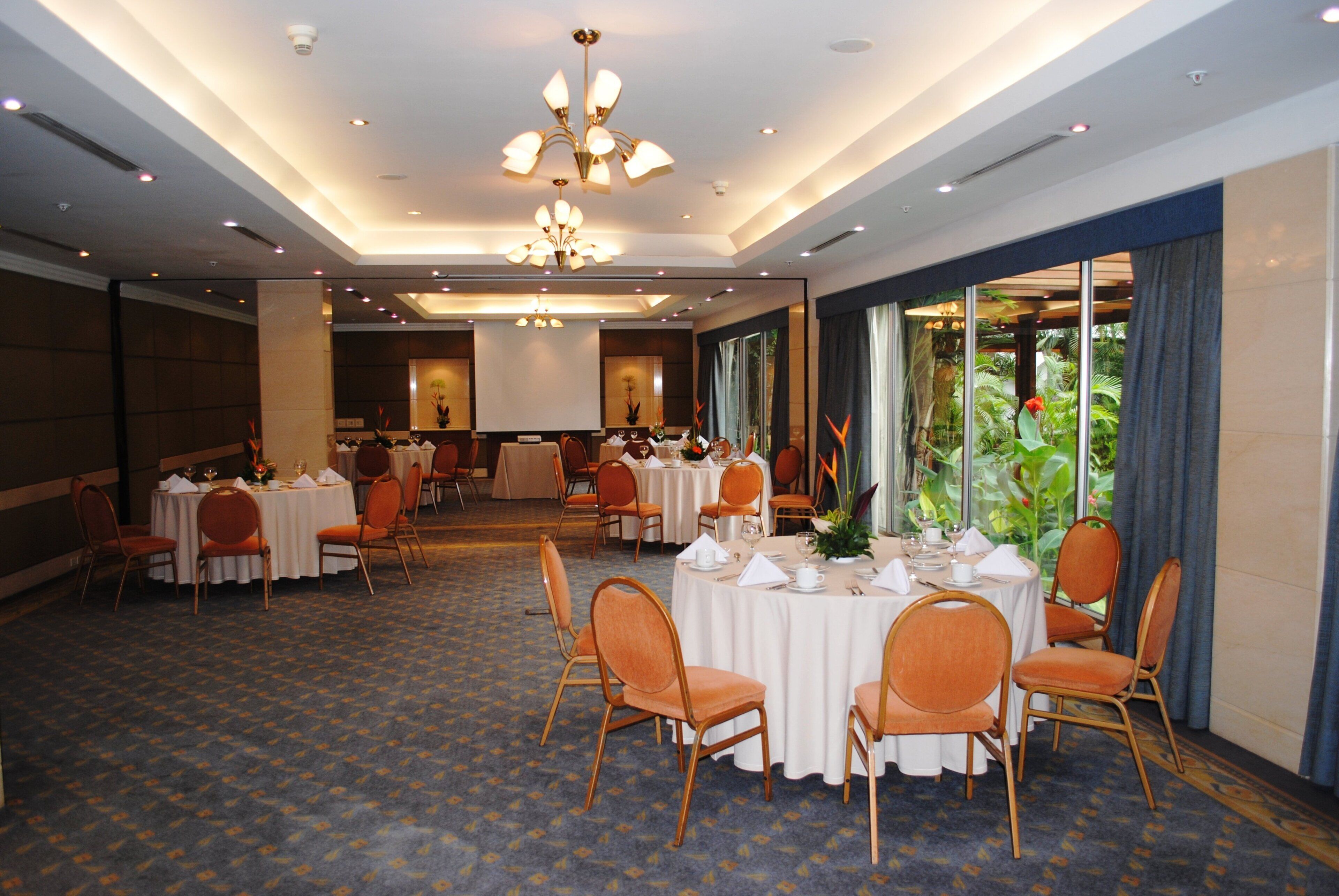 Une salle de banquet avec des tables rondes, des chaises et une grande fenêtre donnant sur un paysage verdoyant.