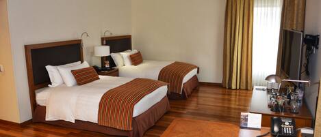 A hotel room with two beds, a desk, a telephone, and a television.