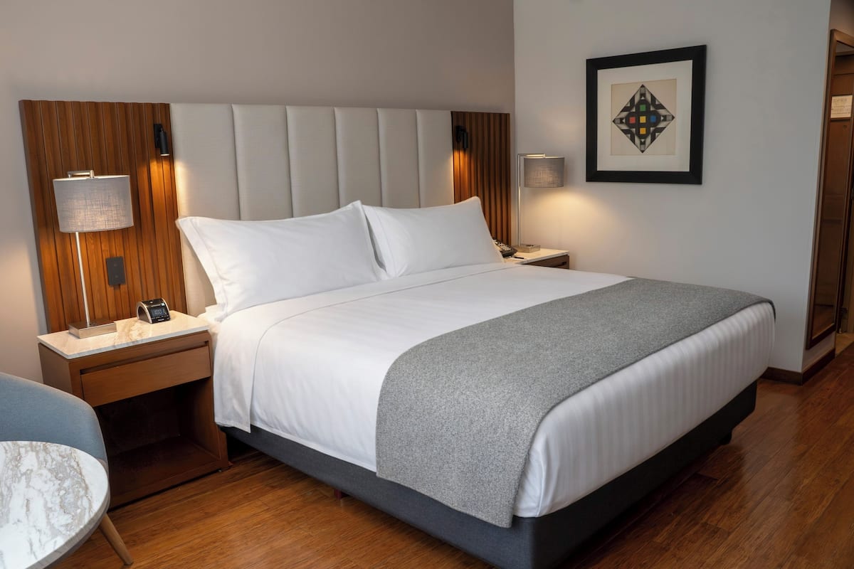 A hotel room with a bed, nightstands, a lamp, a framed picture, and a chair.
