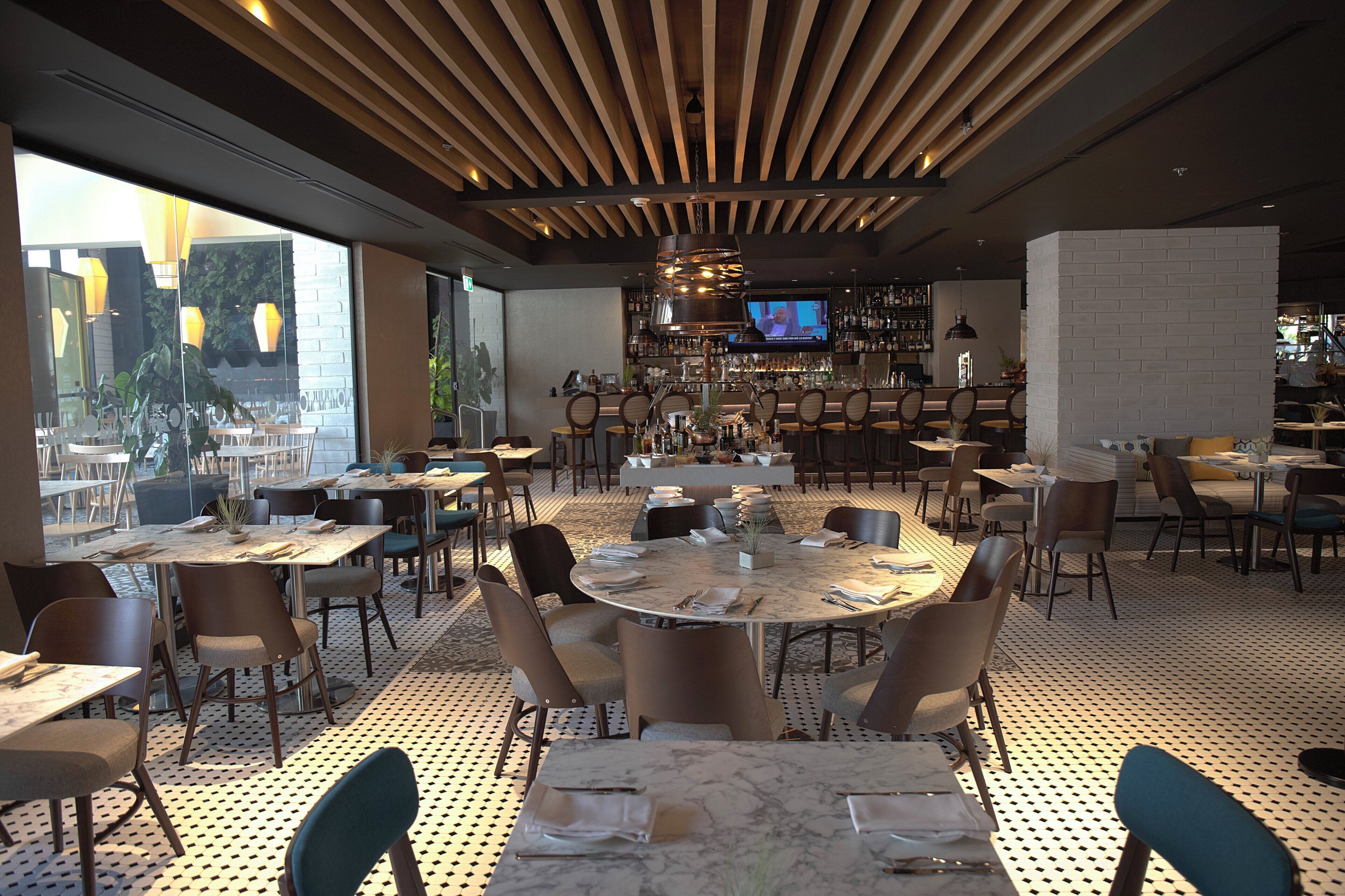 Un restaurante con mesas redondas, sillas, una zona de bar y una pantalla de televisión.