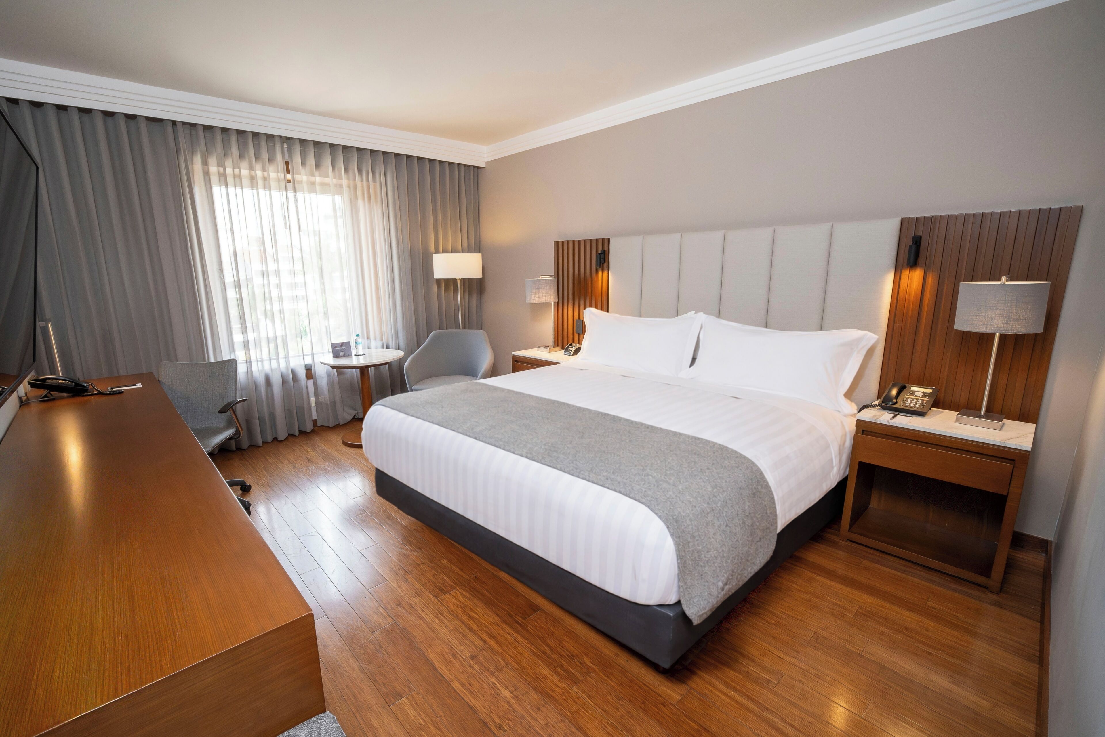 Een hotelkamer met een groot bed, een bureau, een stoel, een klein tafeltje en een lamp.