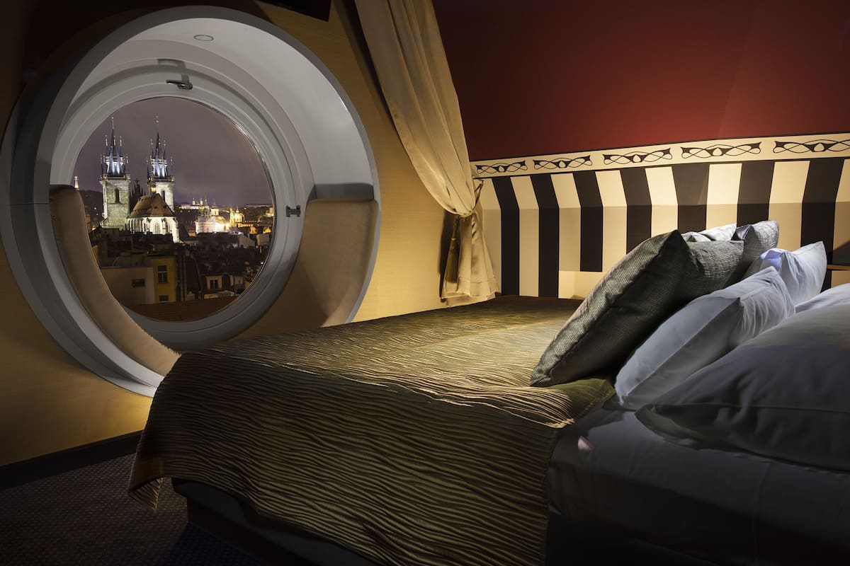 A hotel room with a large round window offering a view of a historic building at night.