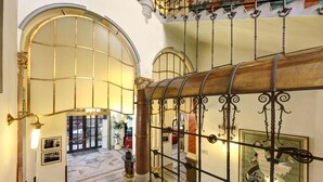 A grand staircase with ornate metal railings and a polished wooden handrail, leading to a lobby area with arched doorways and a tiled floor. - Hotel Paris Prague (Prague)