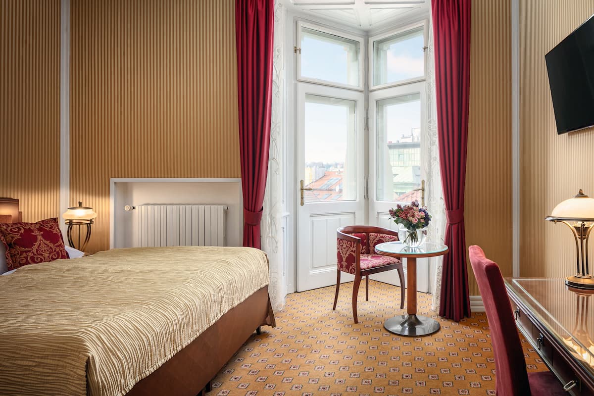 A hotel room with a bed, a small table with a vase of flowers, a chair, and a TV mounted on the wall.