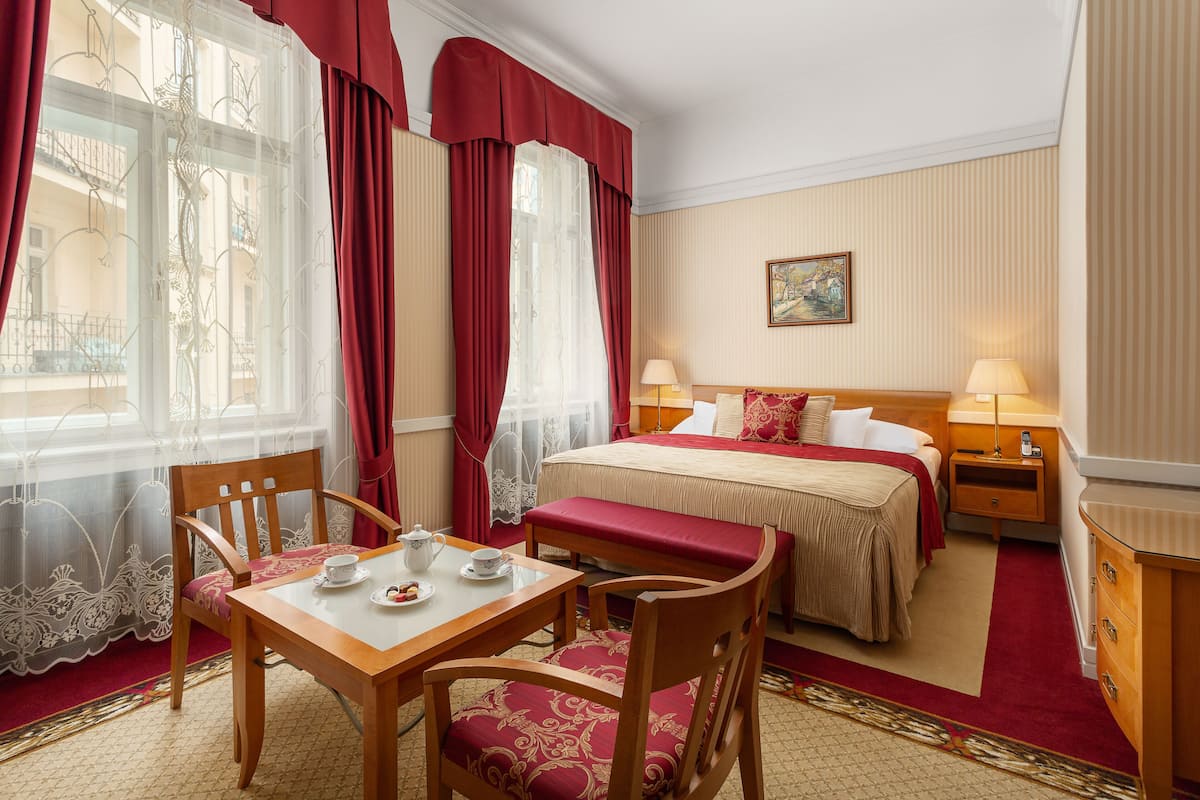 A hotel room with a bed, bedside tables, a desk with a chair, and a window with curtains.