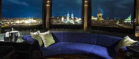 Una habitación moderna con un sofá azul curvo, una mesa de centro de vidrio y vistas nocturnas a lugares emblemáticos de la ciudad.