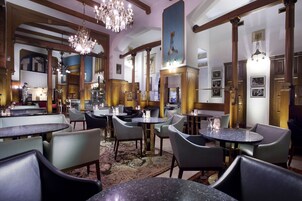 Um saguão de hotel com mesas e cadeiras redondas, um candelabro e um espelho grande.