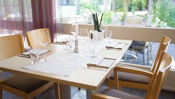 A dining table set with glassware, plates, and cutlery, with chairs around it.