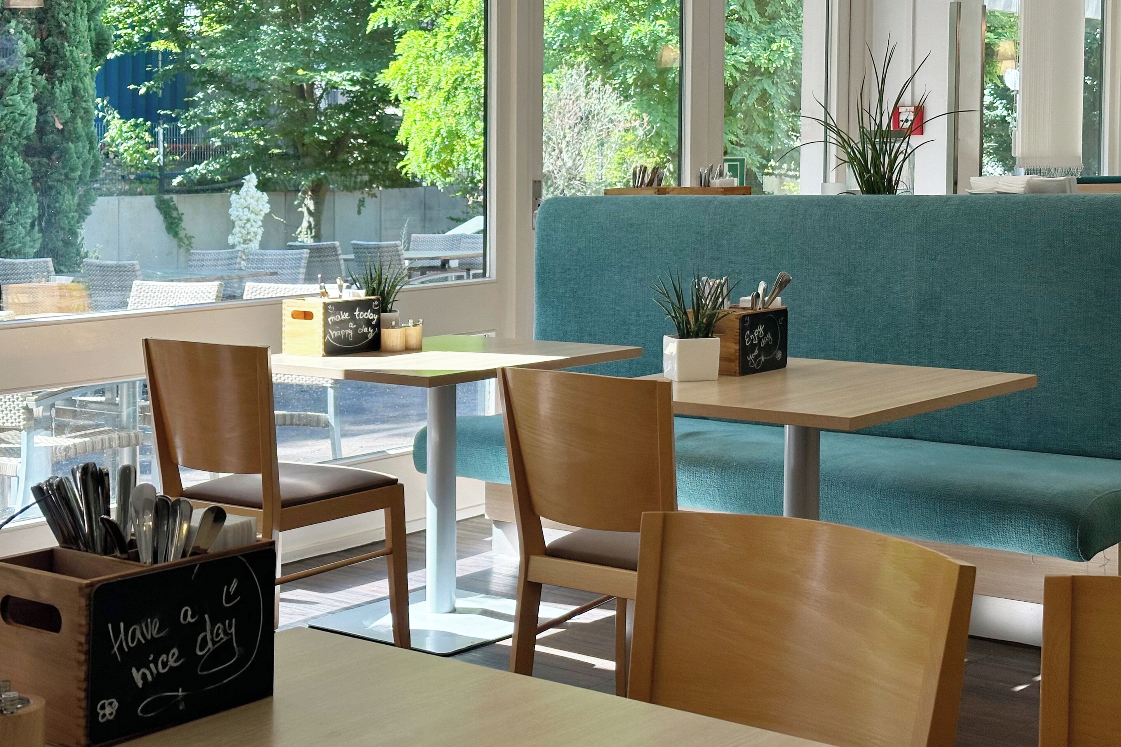 Un accogliente caffè con mobili in legno, una panca imbottita color petrolio e una lavagna con la scritta 'Have a nice day'.