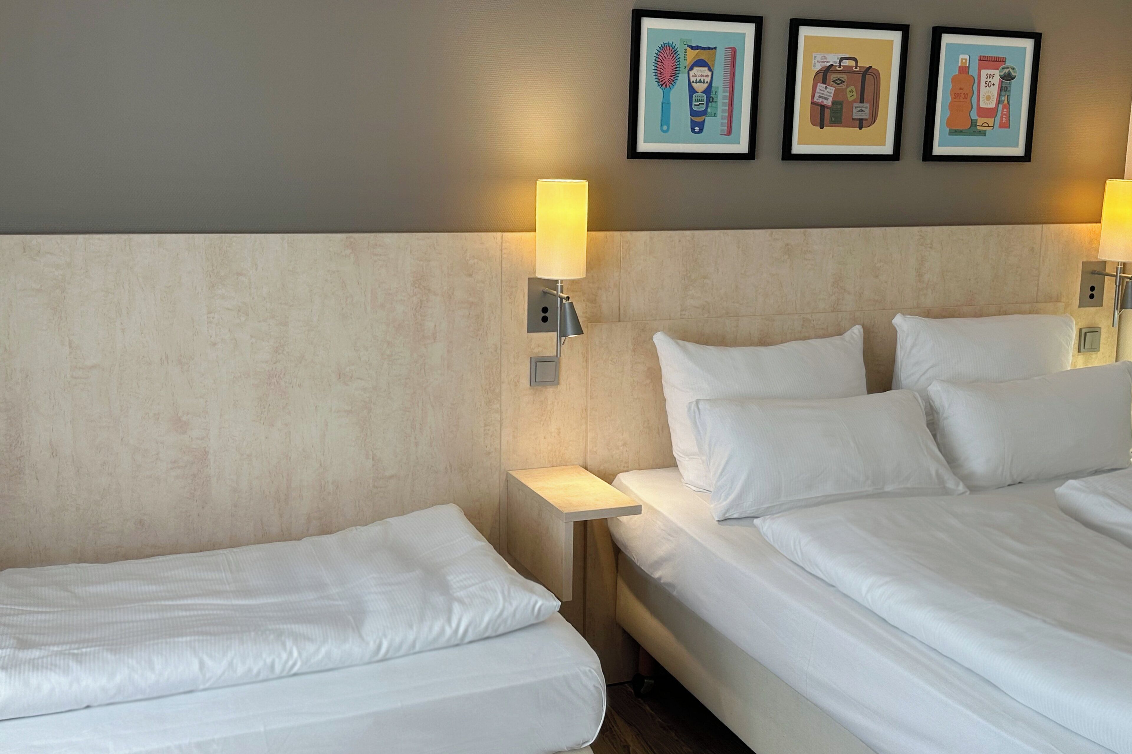 Habitación de hotel con dos camas, cabeceros, lámparas de noche y tres cuadros en la pared.