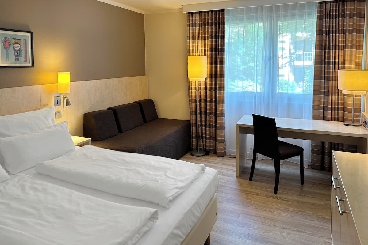 A hotel room with a bed, a desk, a chair, and a sofa.