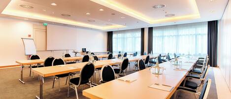 A conference room with multiple tables and chairs, a whiteboard, and a large window with curtains.