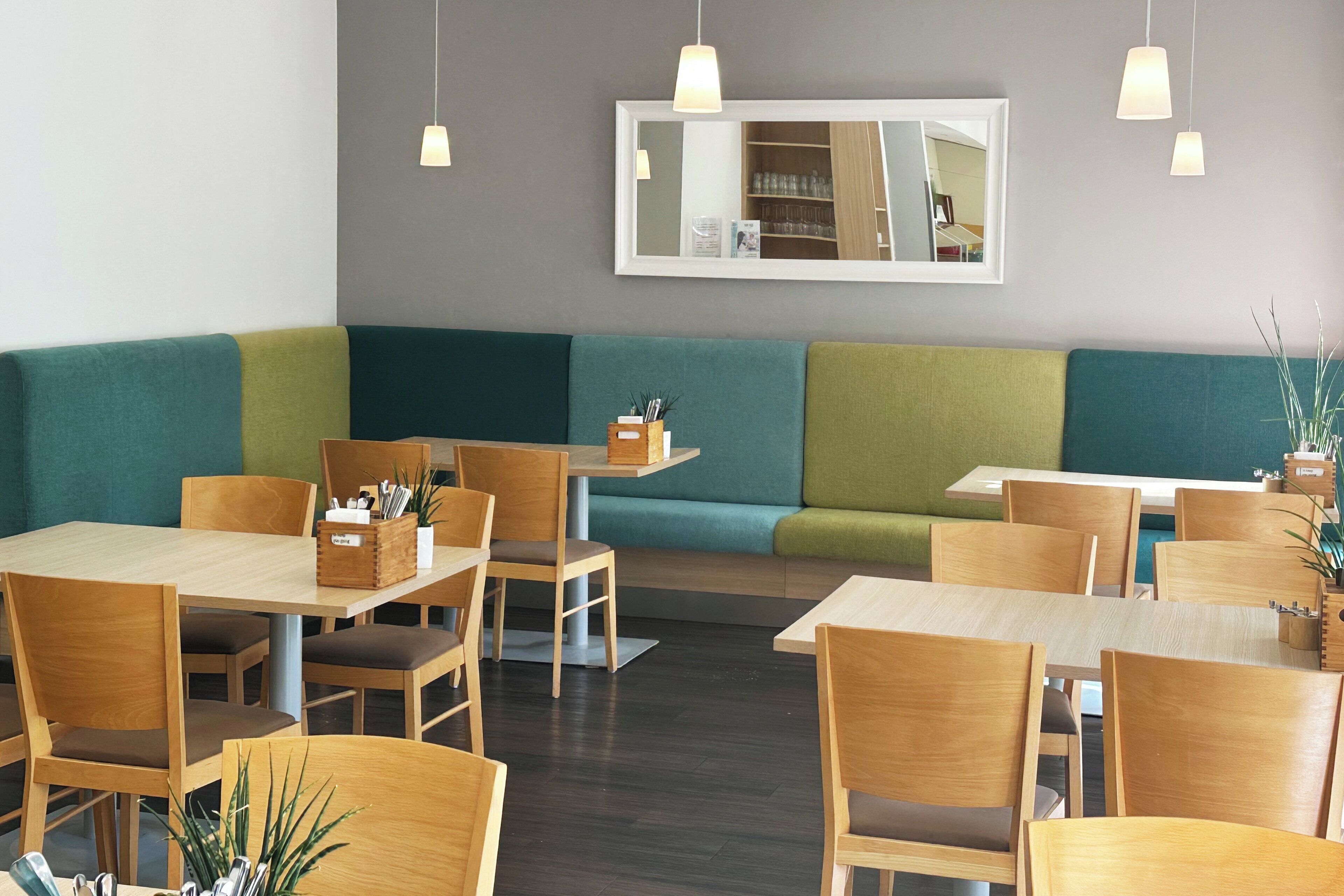 Un restaurante con mesas y sillas de madera, asientos acolchados verdes e iluminación colgante.