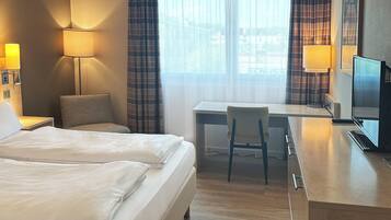 A hotel room with two beds, a desk, a chair, a TV, and two lamps.