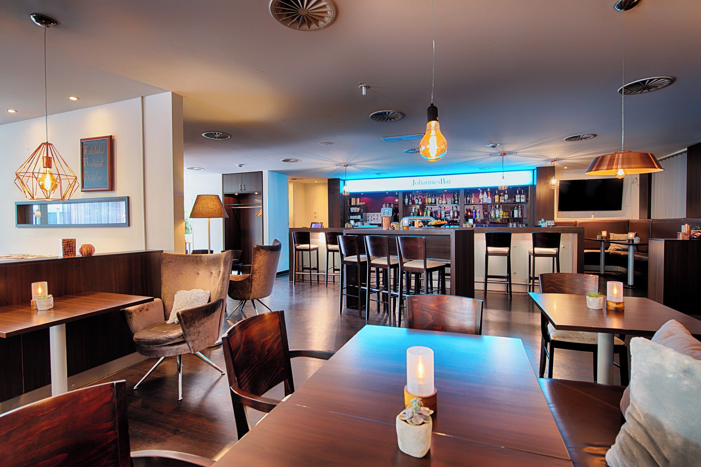 A modern bar area with wooden furniture, a bar counter, and a television screen.