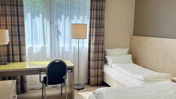 Una habitación de hotel con cama, escritorio, silla, lámpara y cortinas.