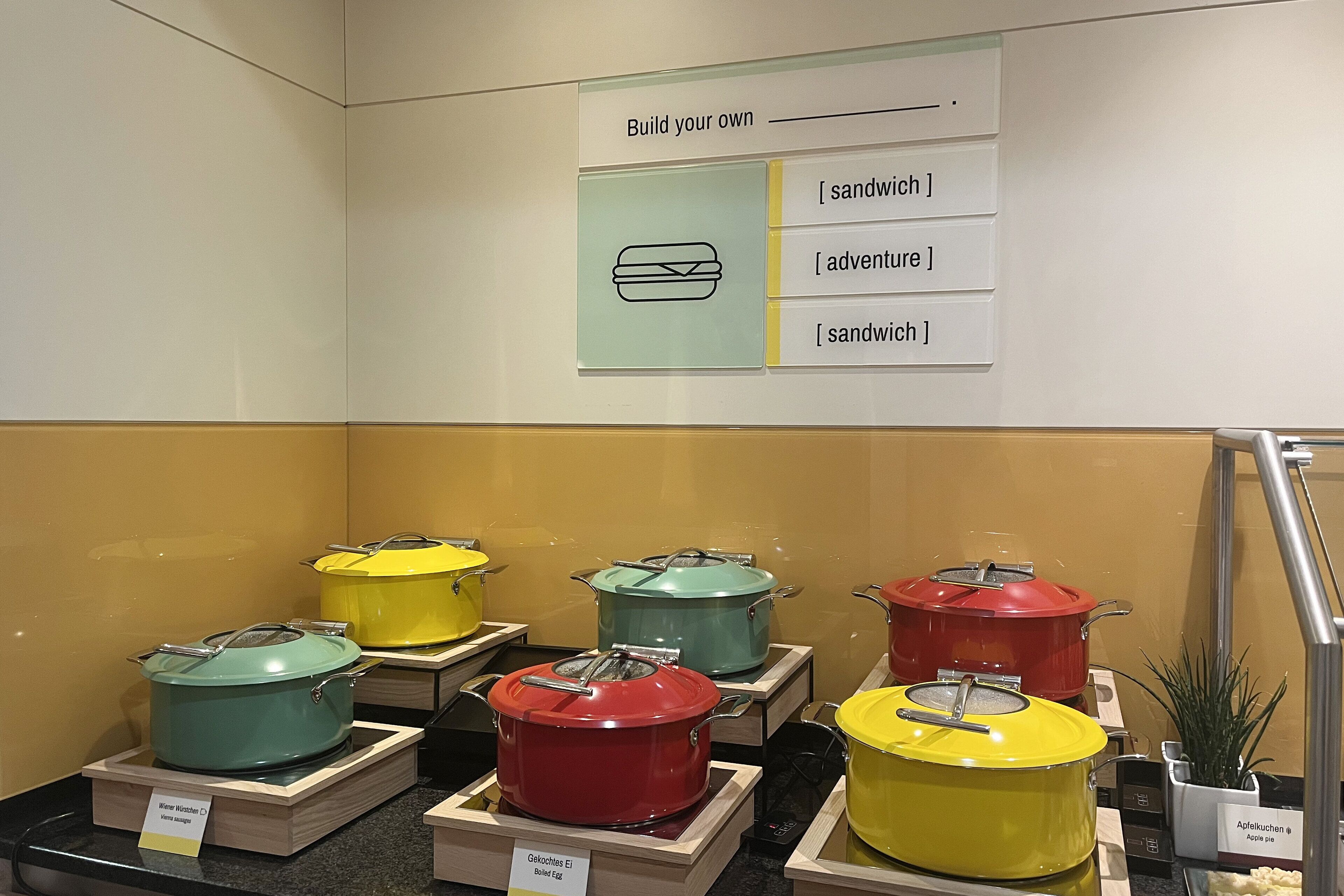 A buffet area with colorful pots labeled 'Gelochtes Ei' and 'Apple Kuchen'.