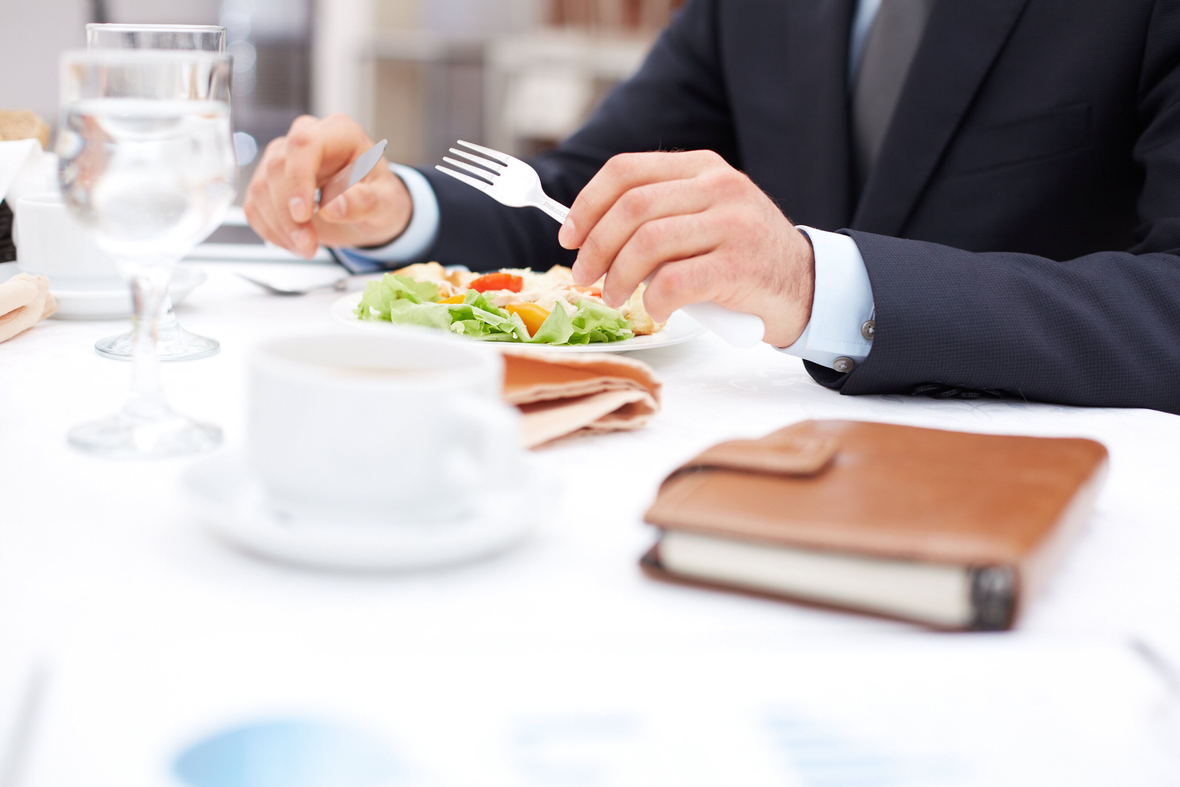 A person in a suit dining at a table with a salad, a glass of water, and a notebook.