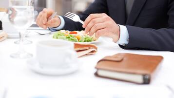 A person in a suit dining at a table with a salad, a glass of water, and a notebook.