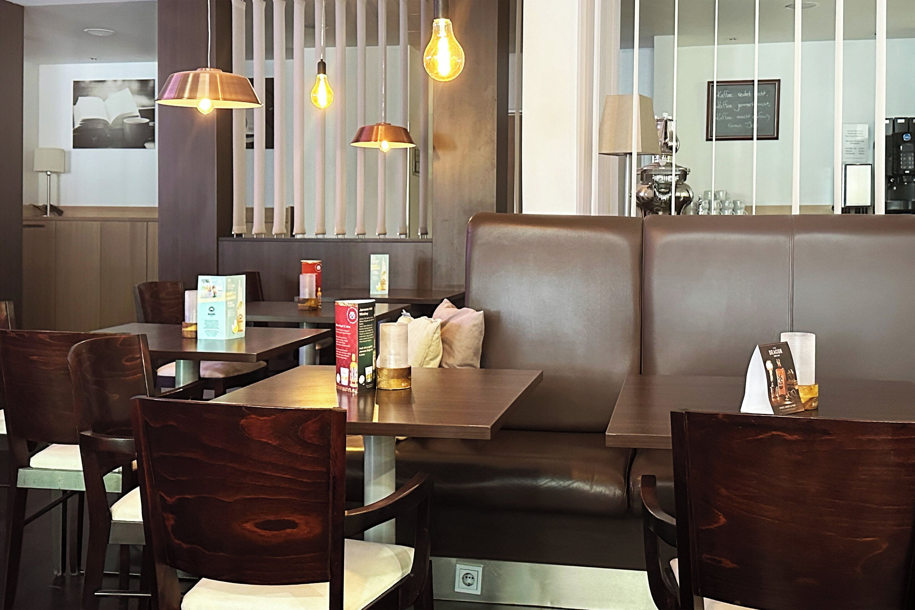 A restaurant interior with wooden tables and chairs, a booth seating area, pendant lighting, and a chalkboard menu.