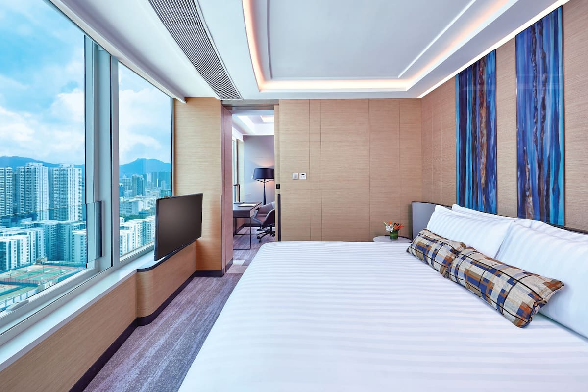A hotel room with a large bed, a flat-screen TV, a desk with a chair, and a city view.