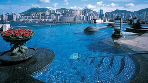 Una piscina con vista a un paisaje urbano, una fuente decorativa y una composición floral.