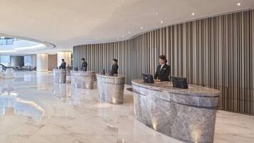 A modern hotel lobby with marble reception counters, a high ceiling, and vertical striped wall panels.