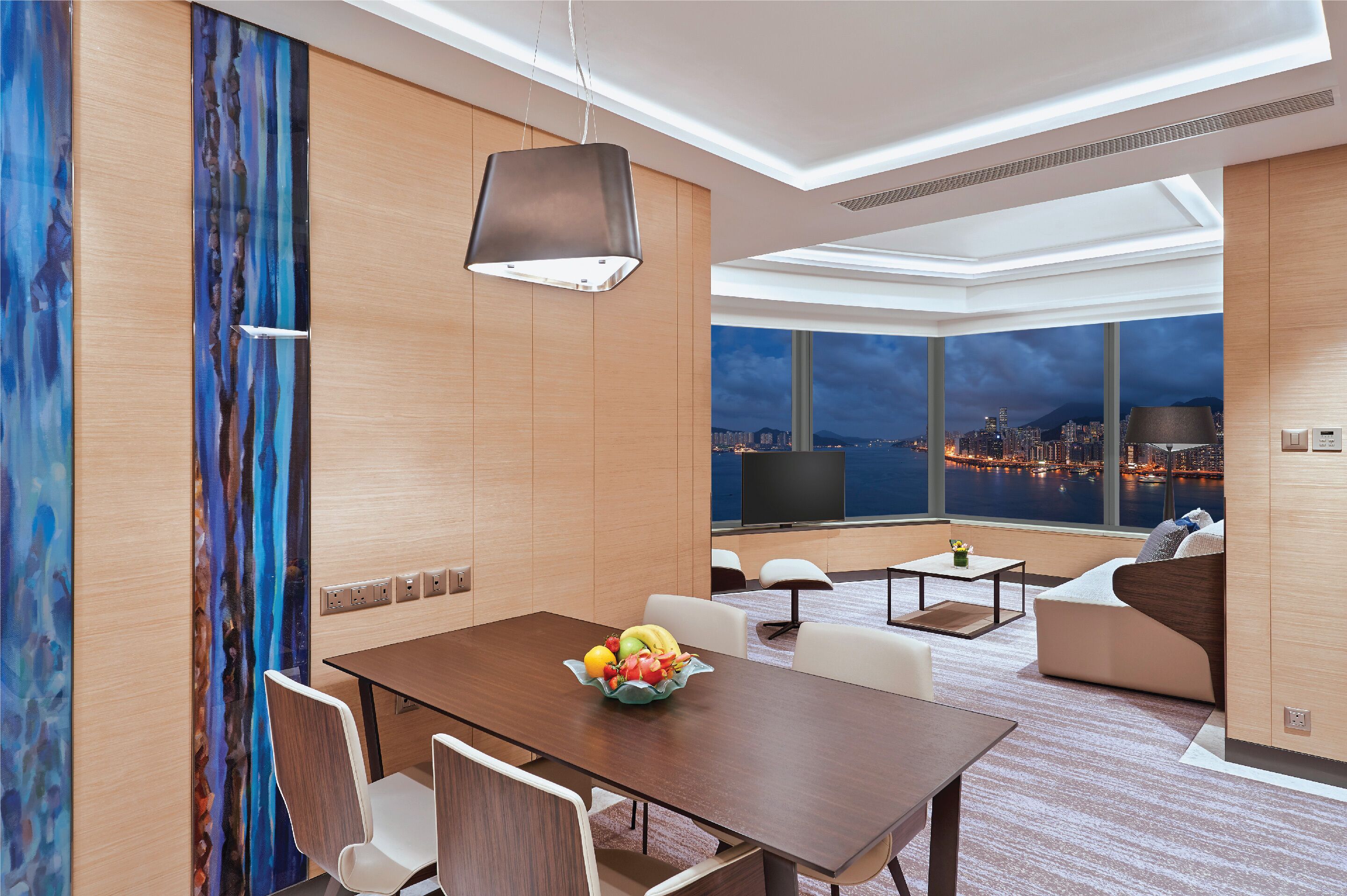 Une chambre d’hôtel moderne dotée d’un coin repas, d’un canapé et d’une grande fenêtre offrant une vue sur la ville.