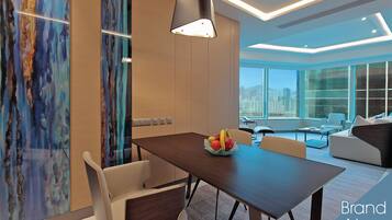 A modern dining area with a wooden table, white chairs, and a fruit bowl. There is a large window with a city view, and the room has a contemporary design with a ceiling light fixture.