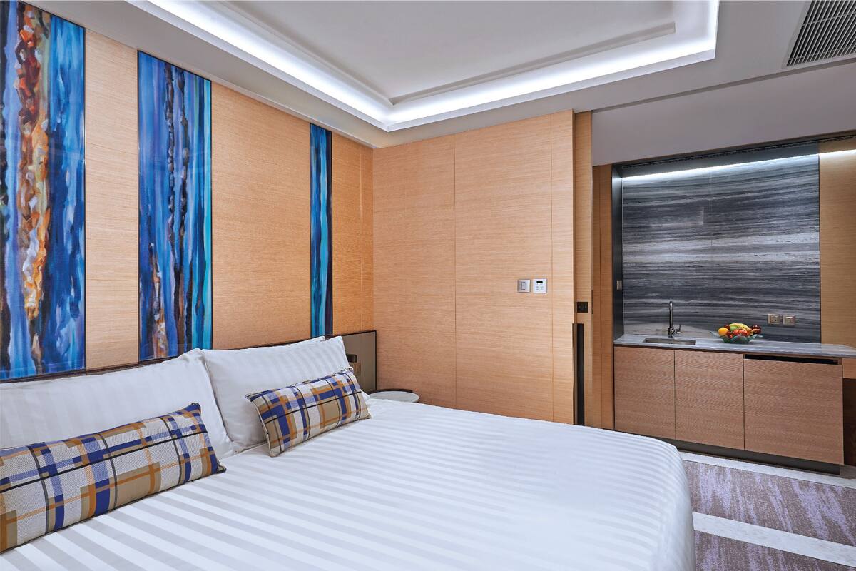 A hotel room with a large bed, a small desk with a sink, and a view of the sea through a large window.