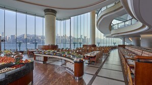 Un comedor amplio con una barra curva, diversas opciones de asientos y vistas a un horizonte urbano a través de grandes ventanales.